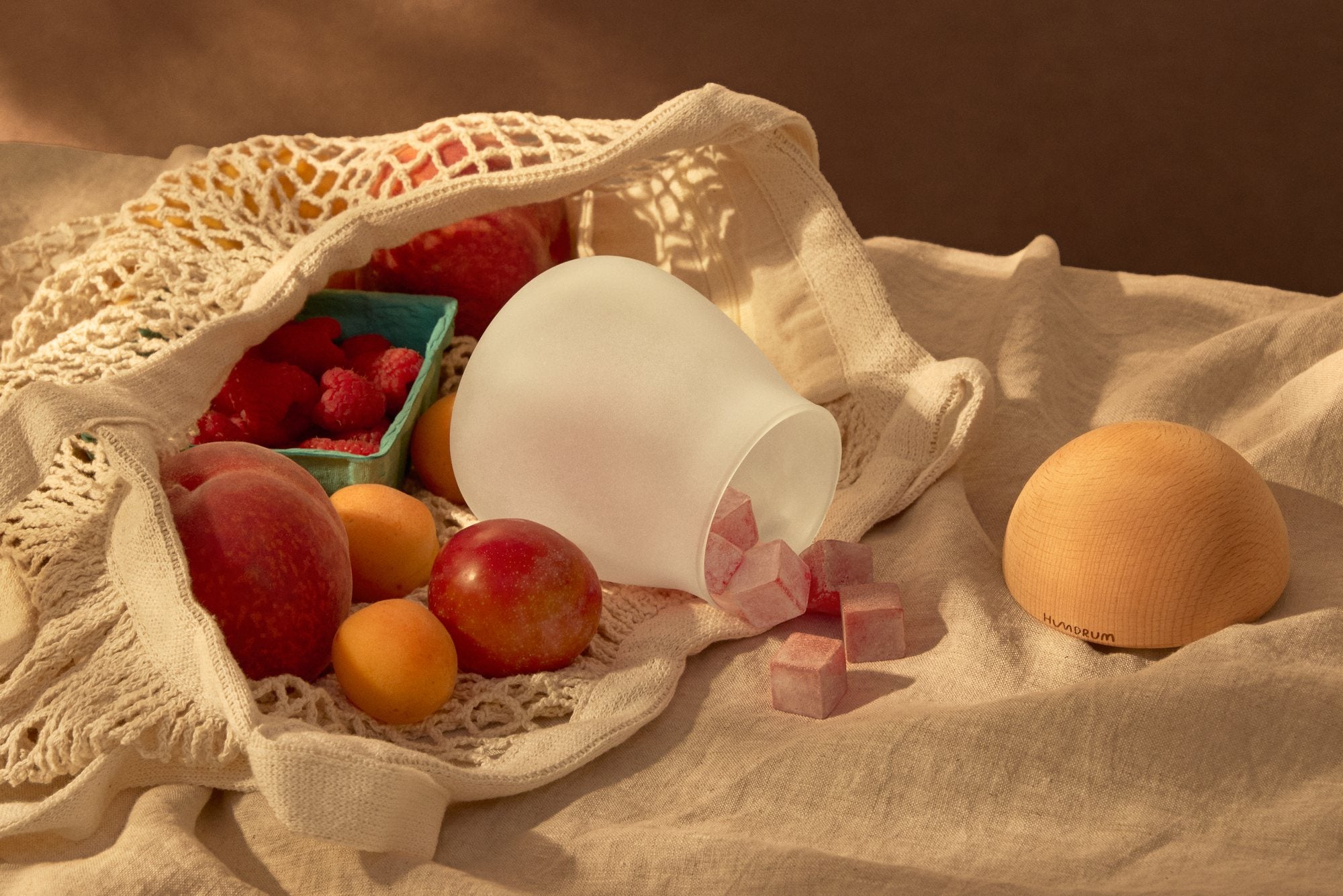 A market bag of stone fruit and raspberries beside a tipped Humdrum jar, chews spilling out