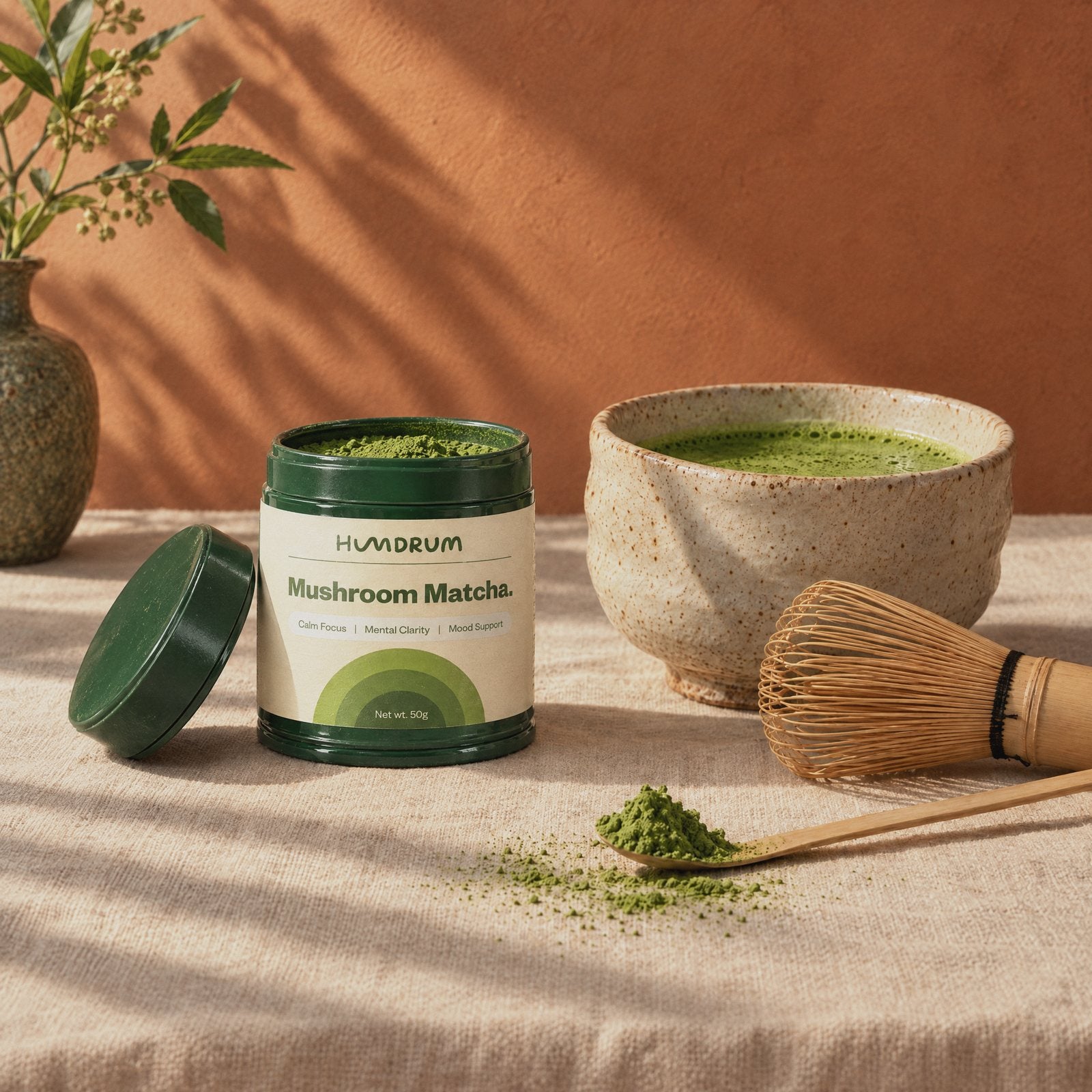 An open tin of Humdrum Mushroom Matcha beside a whisked bowl, bamboo whisk and a scoop of powder