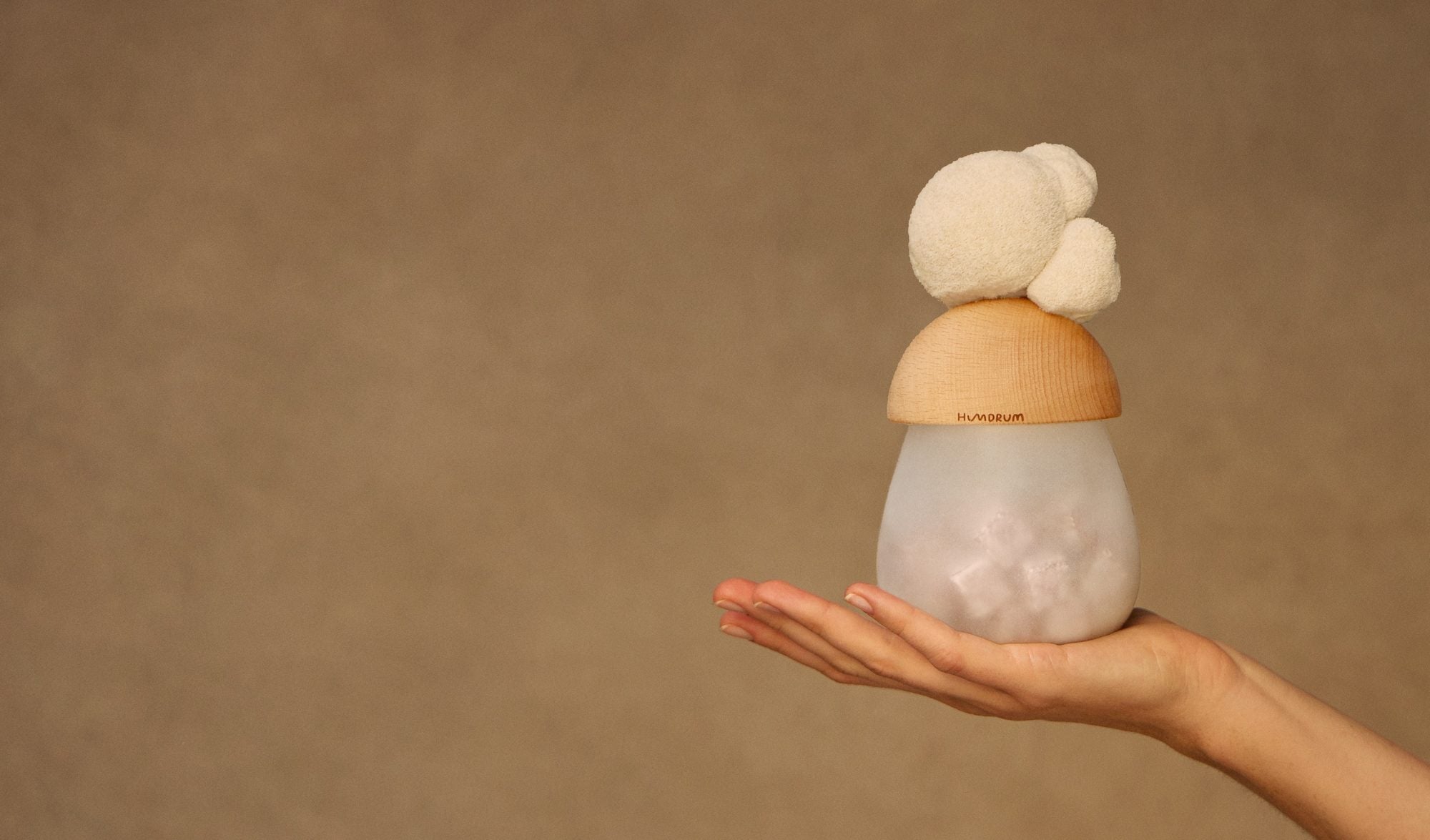 A hand holding a Humdrum jar with a lion's mane mushroom resting on its wooden lid